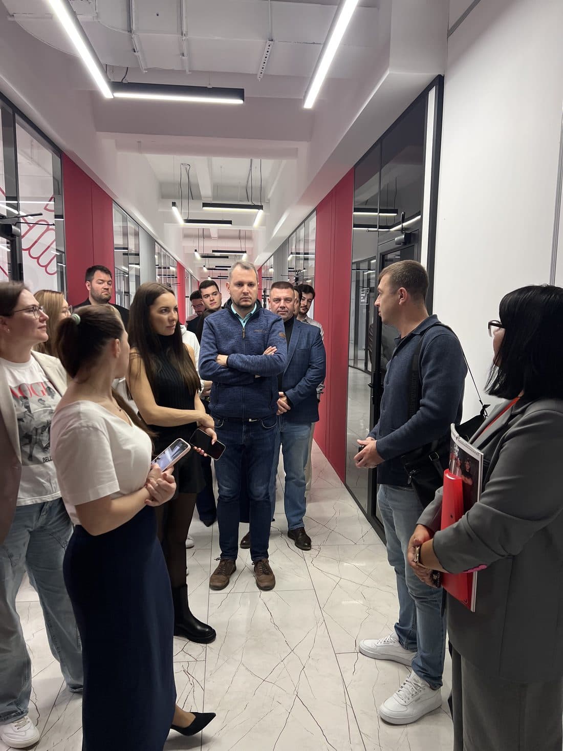 Группа участников слушает в коридоре офиса АКФИКС с красными стенами