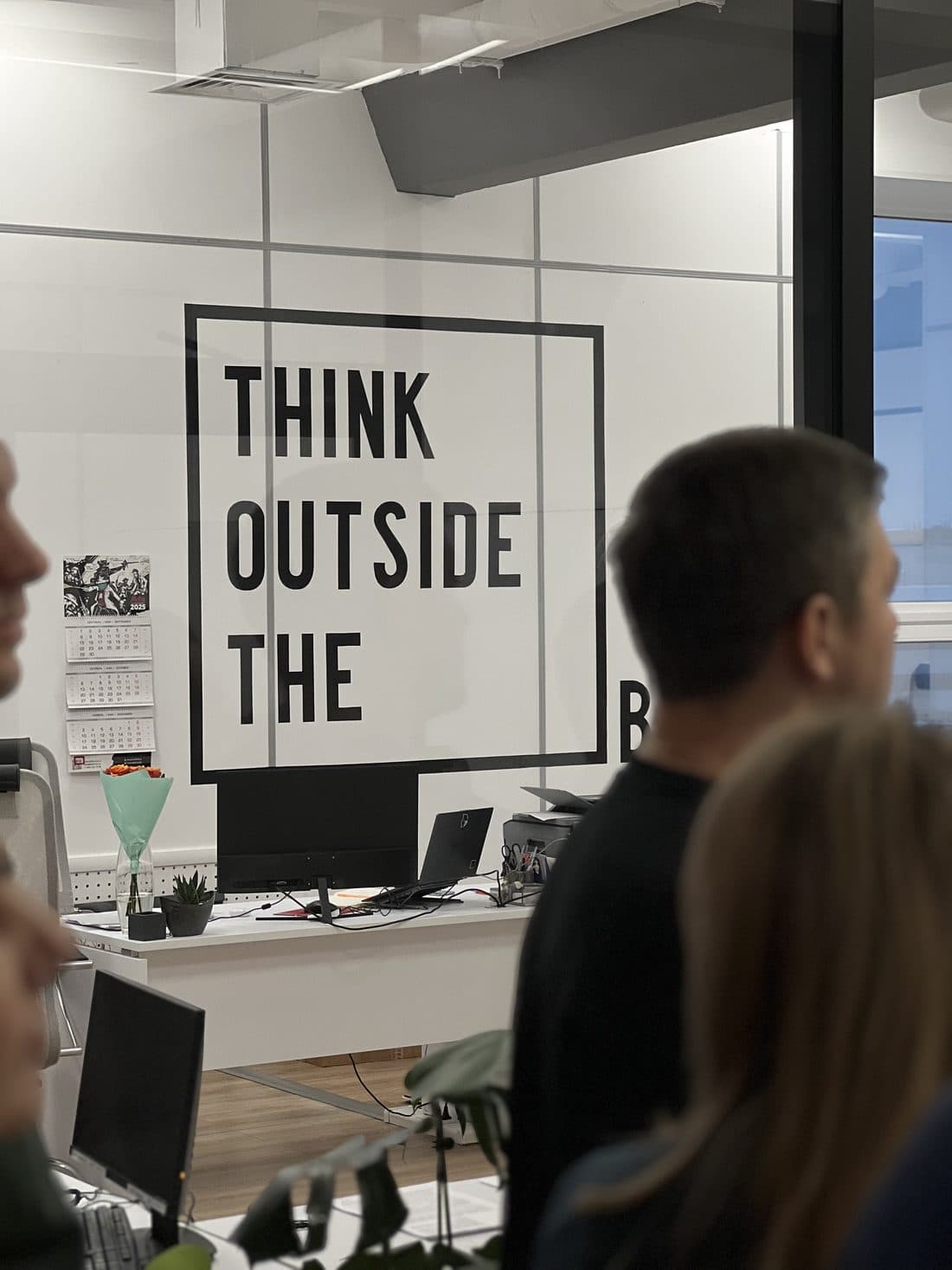 Участники у стеклянной перегородки опенспейса с надписью Think outside the box