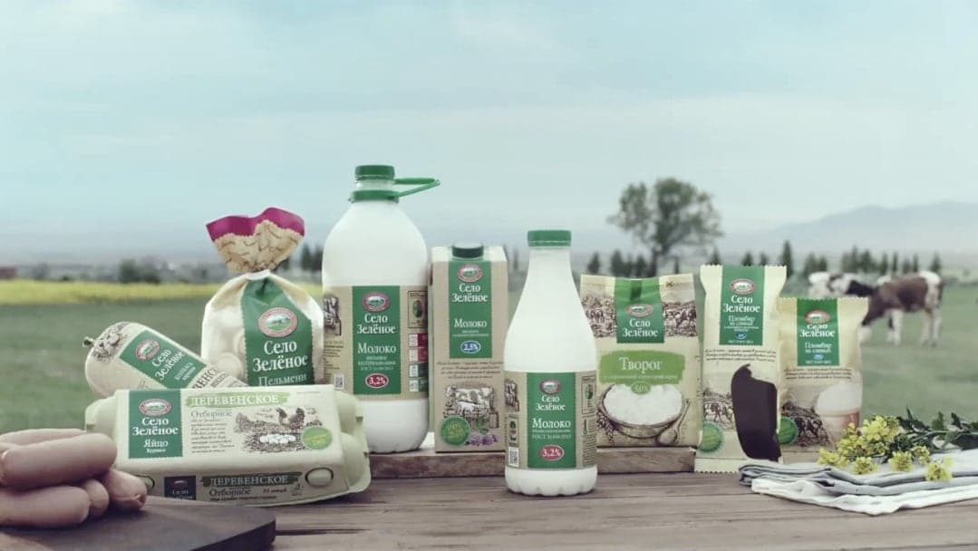 Продукция «Село Зелёное»: молоко в бутылках, творог и другие продукты на траве, вдали пасутся коровы